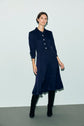 A person wearing a bleu marine, long-sleeved robe midi with col chemise and buttons, paired with black knee-high boots, stands against a plain light grey background.