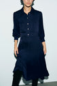 A person wearing a bleu marine, long-sleeved robe midi with a col chemise stands against a light background. Their face is partially out of frame.