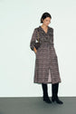 Woman wearing an imprimé graphique, long-sleeve robe midi with a ceinture à nouer, paired with a black crossbody bag and black knee-high boots, standing against a light background.