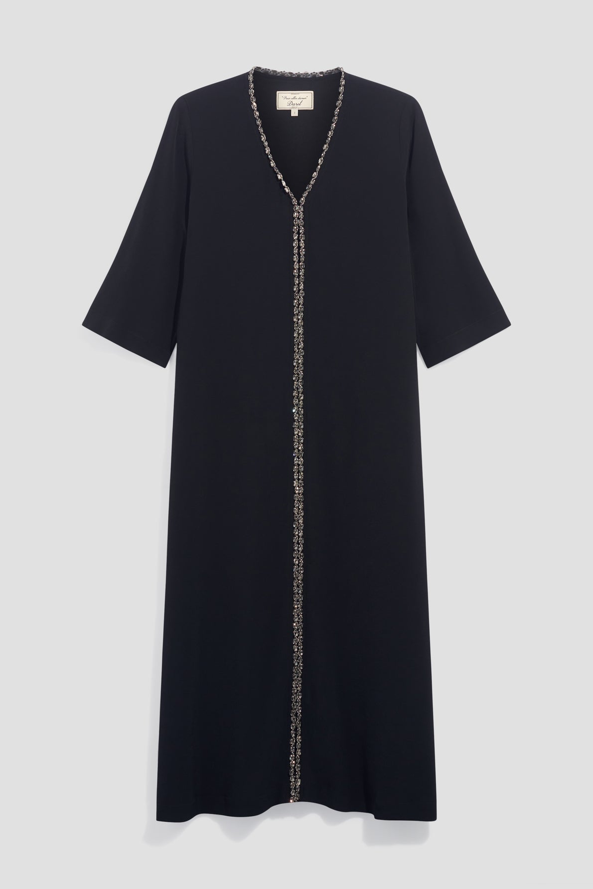 A black, knee-length dress with three-quarter sleeves and a V-neckline. Reminiscent of a caftan noir, it features a decorative trim running down the center from the neckline to the hem. The dress is displayed on a plain light gray background.