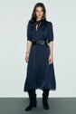 A woman stands against a plain background wearing a navy robe midi satin with a keyhole neckline, black belt, and black knee-high boots.