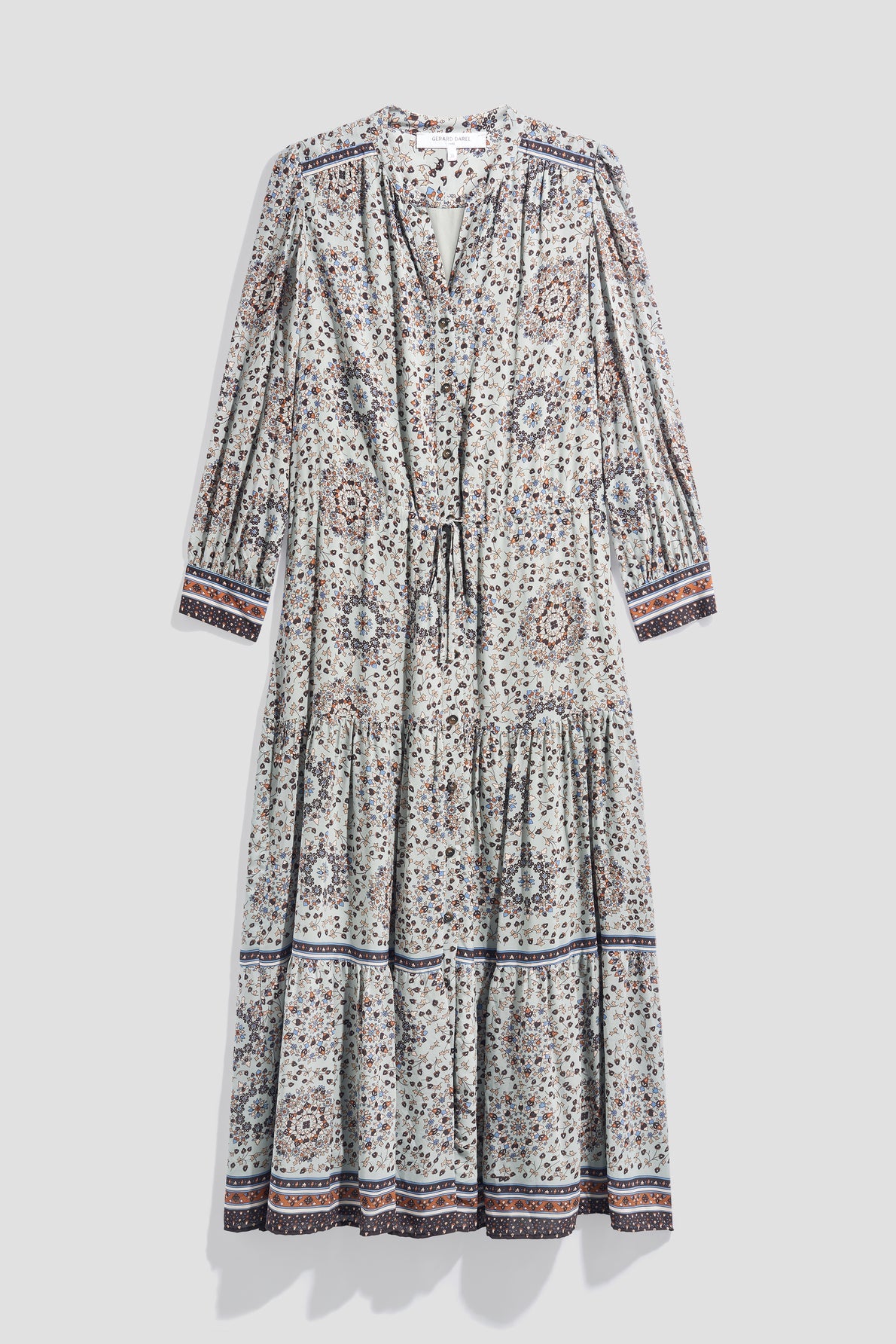 Long-sleeve, ankle-length robe longue with an imprimé floral and geometric pattern, featuring a tie at the neckline and tiered skirt. The dress has a white base with blue, brown, and purple accents on the cuffs and hem.