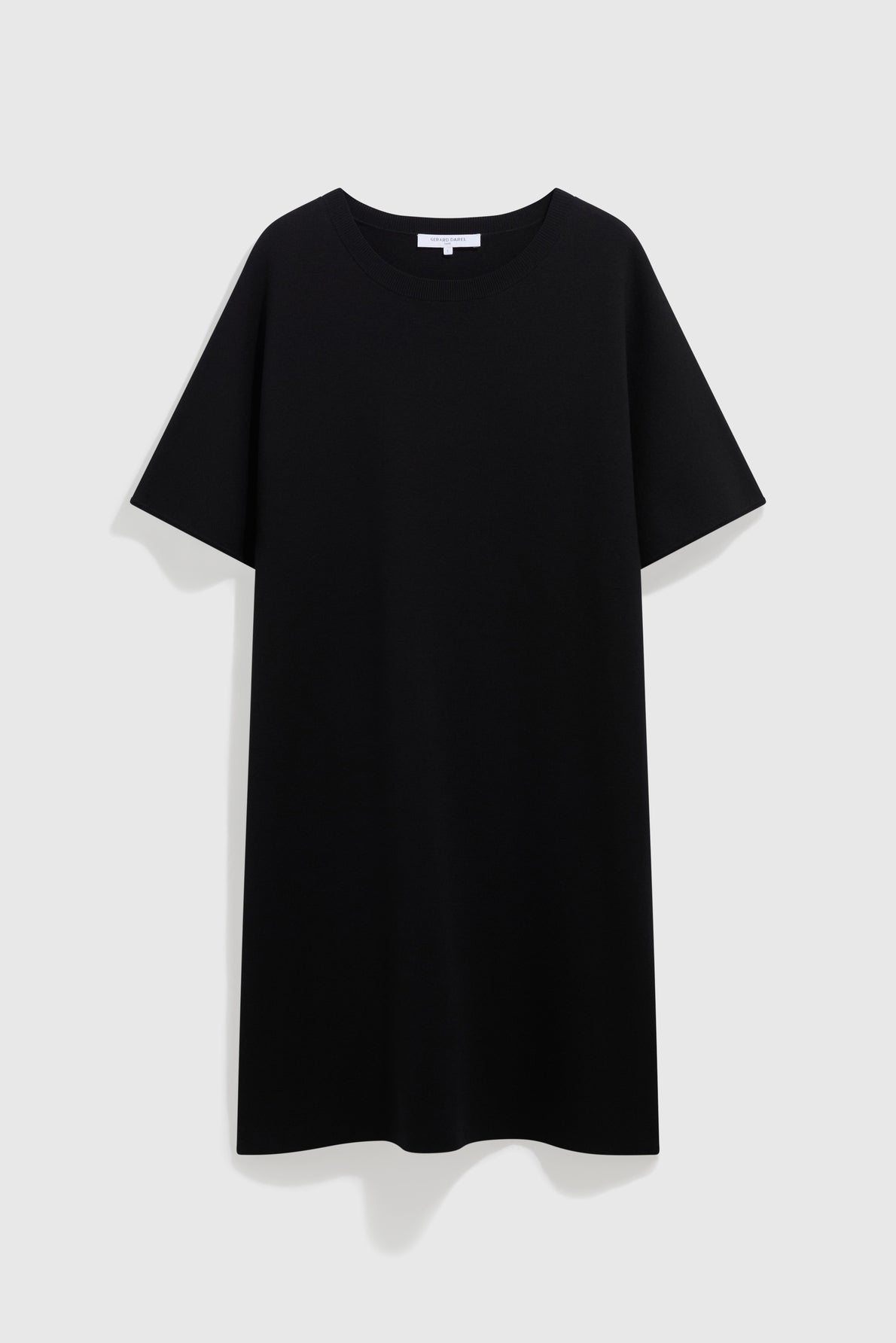 A plain black short-sleeve T-shirt dress in maille Milano is displayed on a light gray background, offering the effortless elegance of a robe courte.