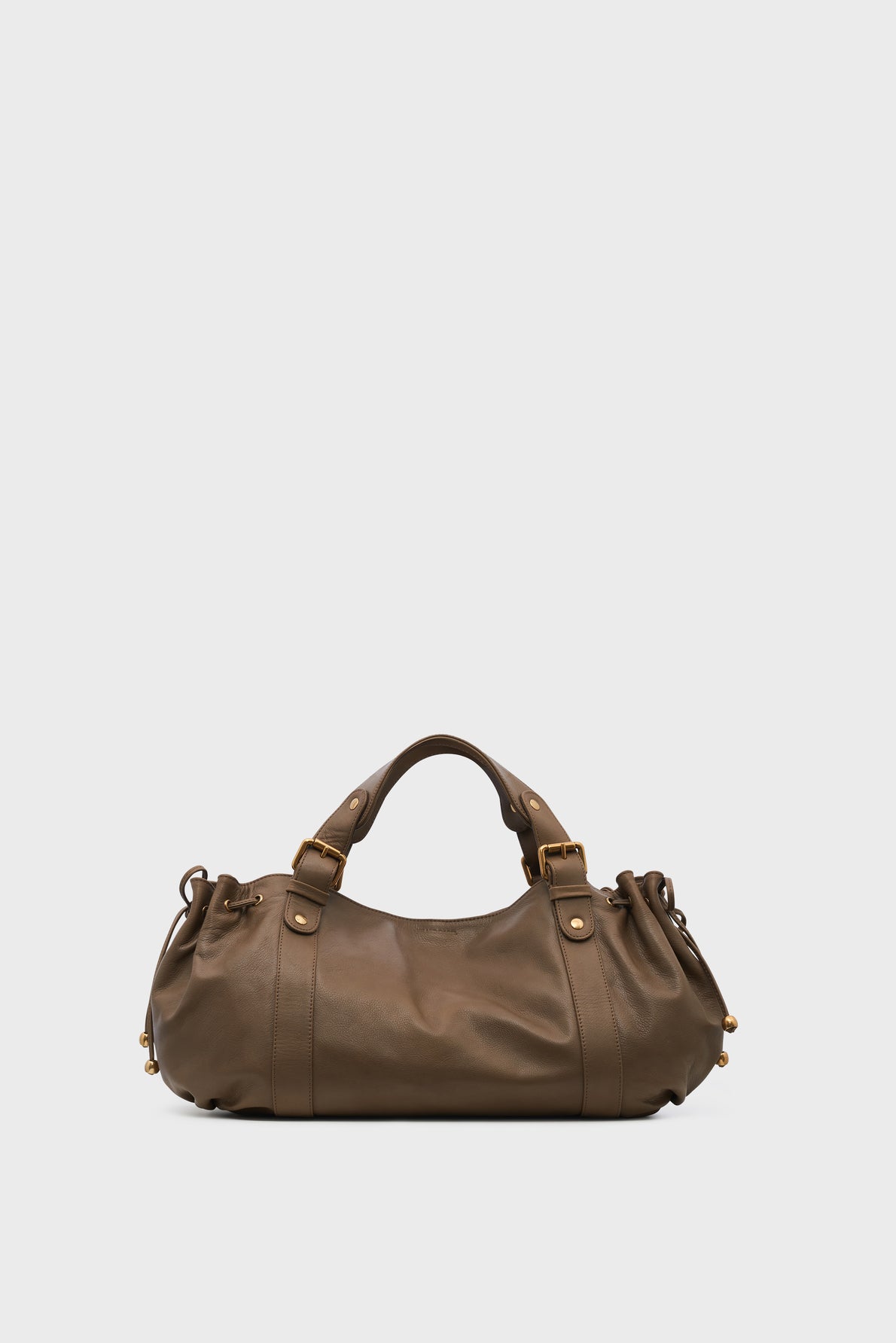 A brown leather sac à main cuir with two short handles, gold hardware, and gathered detailing on the sides, set against a plain light gray background, exemplifying timeless maroquinerie Darel craftsmanship.