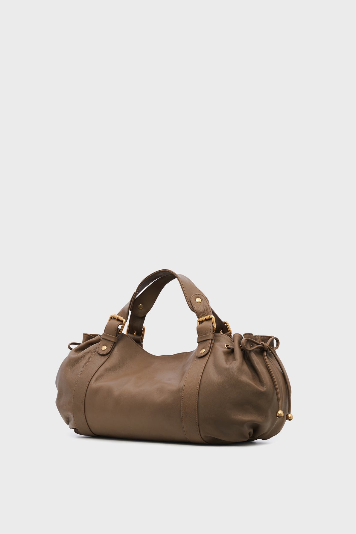 A brown leather sac à main cuir with gold hardware, double handles, and gathered side details, placed against a plain light gray background.