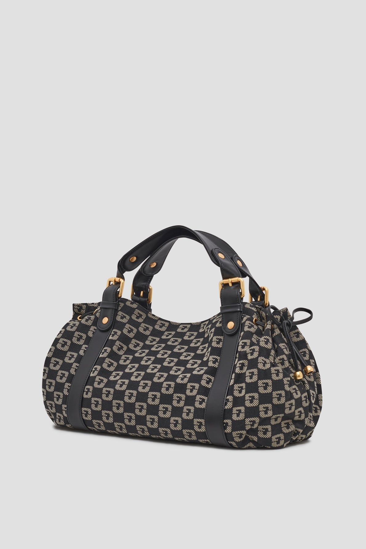 A cylindrical sac à main jacquard with black leather handles and trim, featuring a black and beige geometric pattern evocative of a sac monogrammé and gold-tone hardware, set against a plain light background.
