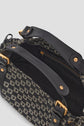 A close-up of an open black sac à main jacquard with a patterned fabric exterior, gold-tone hardware, black leather straps, and a visible zippered pocket inside.