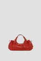 A red leather handbag crafted from luxurious cuir de chèvre, featuring gold hardware, short handles, and a gathered design, sits against a plain light gray background—a timeless sac à main that perfectly showcases the elegance of maroquinerie Darel.
