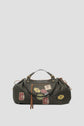 A dark patterned 72H Sac de voyage with tan leather handles and zipper pulls, crafted from durable toile enduite and decorated with colorful vintage-style travel patches on the front, set against a plain light background—perfect for your next escapade Paris.