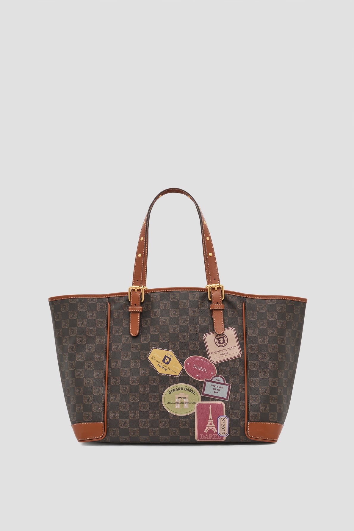 A brown checkered cabas toile enduite tote bag with tan leather handles and corners, decorated with colorful travel-themed patches and tags featuring various destinations and travel motifs.