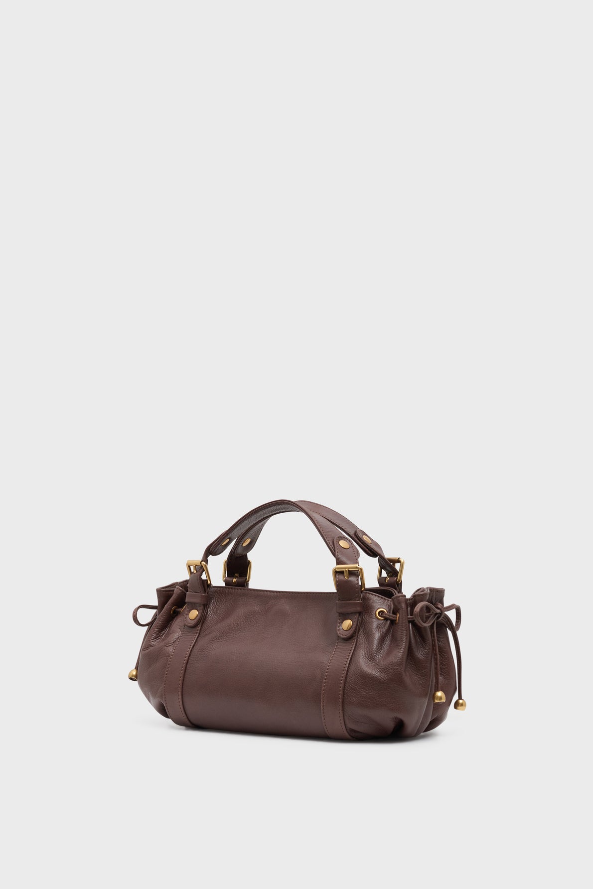 A small brown cuir de vachette sac à main with gold hardware, decorative side ties, and double handles, displayed against a plain light grey background.