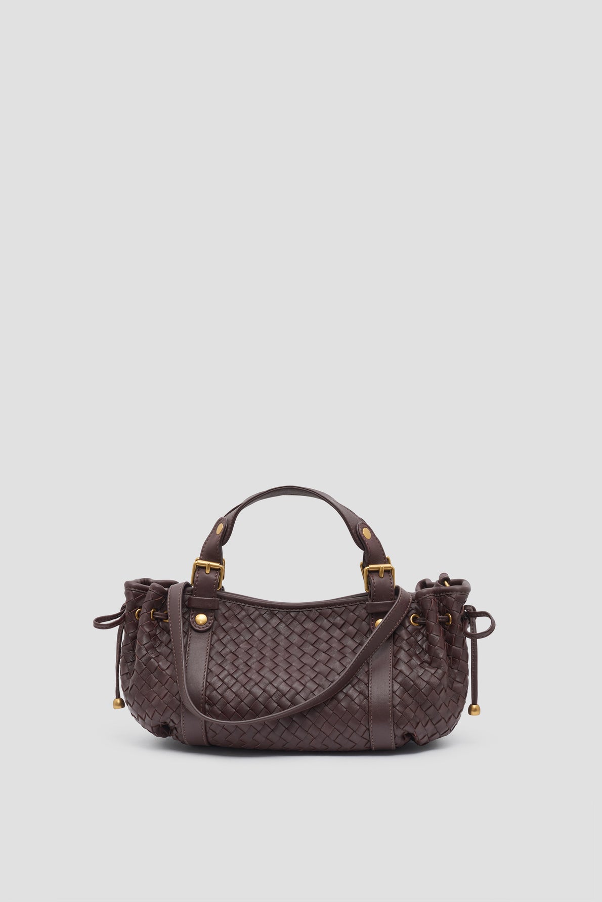 A dark brown sac à main crafted from cuir d’agneau tressé, this it-bag 12H features woven leather, short handles, gold hardware, and side drawstring details, elegantly displayed on a plain light background.