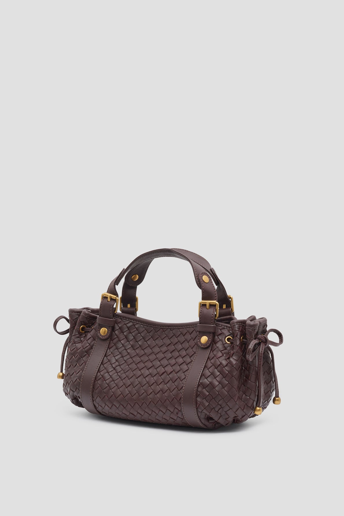Dark brown sac à main crafted from cuir d’agneau tressé with gold hardware, two handles, side drawstrings, and decorative stitching, displayed on a light grey background.