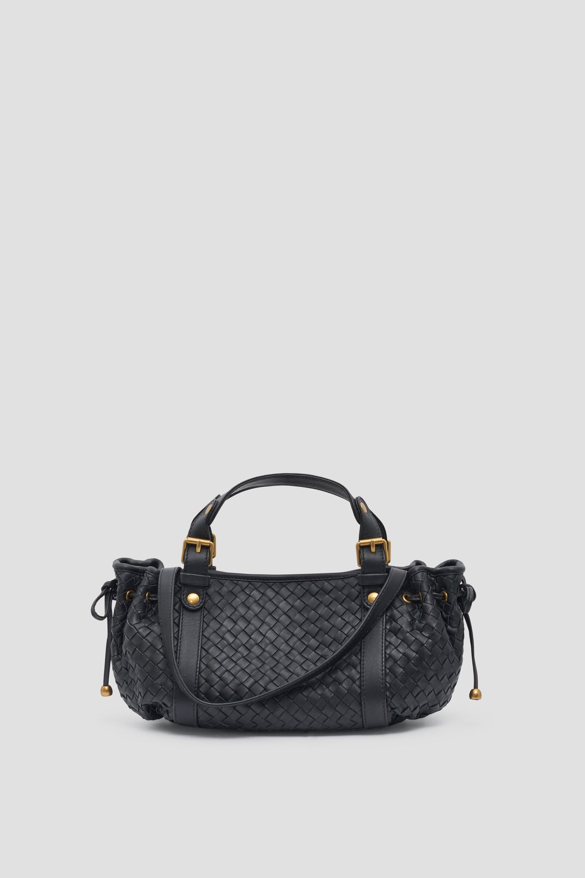 A black sac à main tressé in woven cuir d’agneau leather, featuring two handles, gold hardware, and side drawstring details, displayed against a plain light gray background.