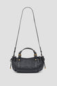 A black cuir d’agneau sac à main tressé with gold hardware, short handles, and a long adjustable shoulder strap, displayed on a plain light background.