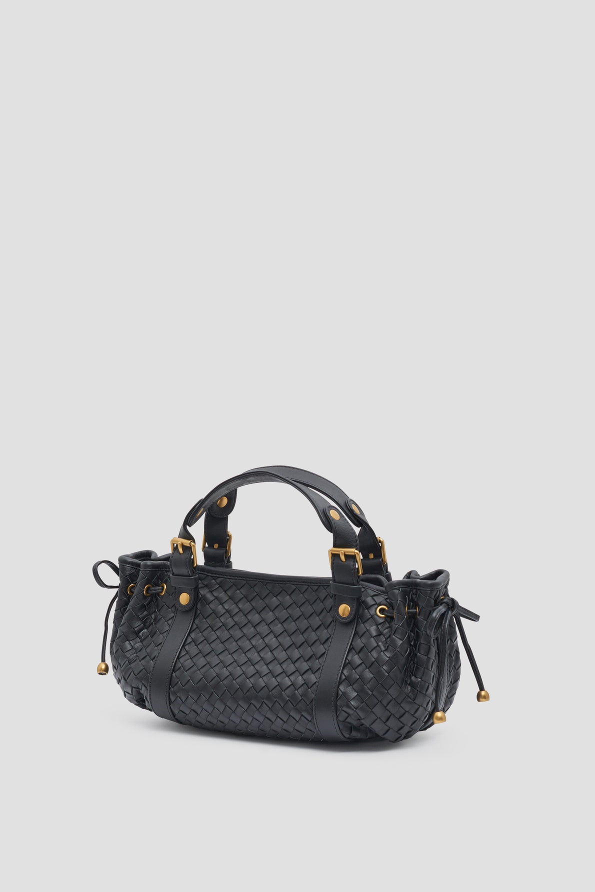 A black sac à main tressé in luxurious cuir d’agneau with gold hardware, two handles, and side drawstring details, the it-bag 12H is displayed against a plain light gray background.