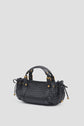 A black sac à main tressé in luxurious cuir d’agneau with gold hardware, two handles, and side drawstring details, the it-bag 12H is displayed against a plain light gray background.