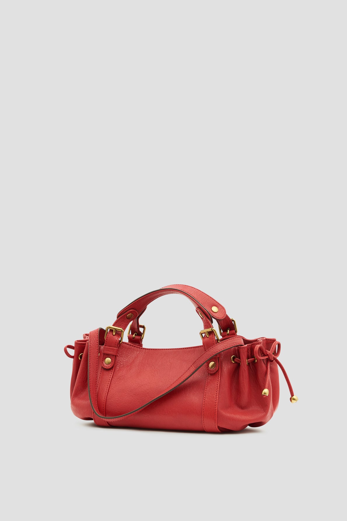 A small red sac à main in luxurious cuir de chèvre with gold hardware, two handles, and drawstring details on the sides, this elegant it-bag 12H is displayed against a plain light gray background.