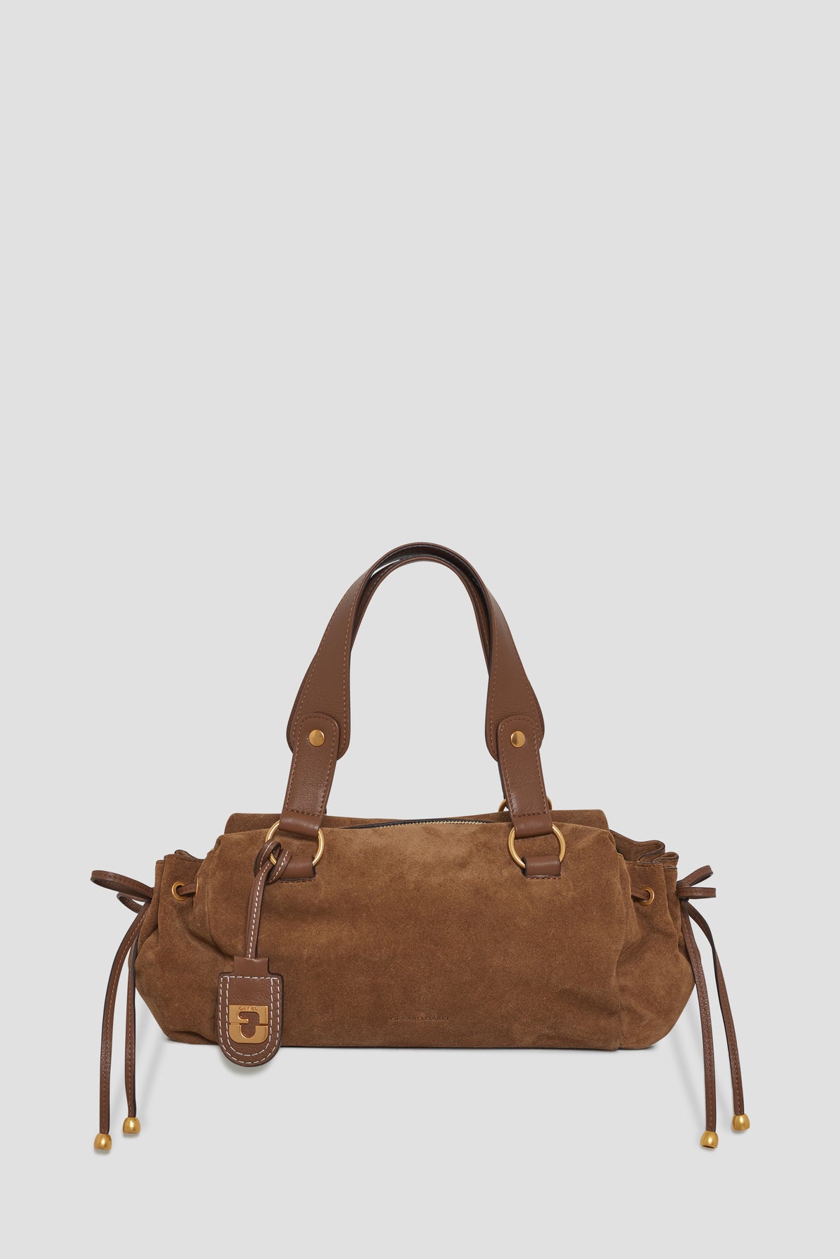 Brown suede handbag (cuir velours) with leather handles and gold hardware, featuring side drawstrings, a fermeture zippée for added security, and a small hanging tag on a plain light gray background.