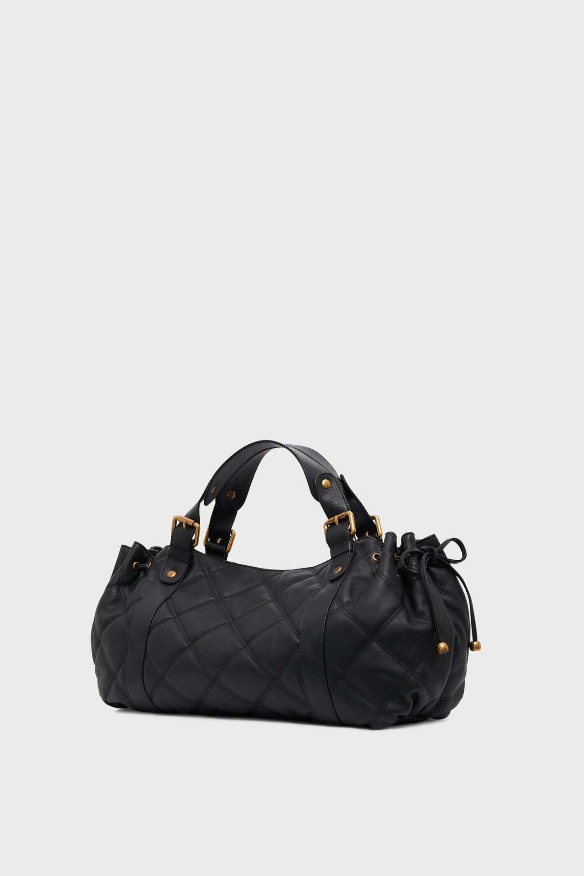 A black version matelassée sac à main in quilted leather with gold hardware, dual handles, and a drawstring detail on one side, beautifully showcasing a savoir-faire d’exception against a plain light background.
