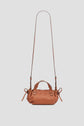 A small brown leather sac bandoulière cuir handbag featuring two handles, side drawstring details, and a long adjustable shoulder strap, displayed against a plain light gray background. Part of the exclusive collaboration Merci collection, this Micro 24 accessory exudes understated elegance.
