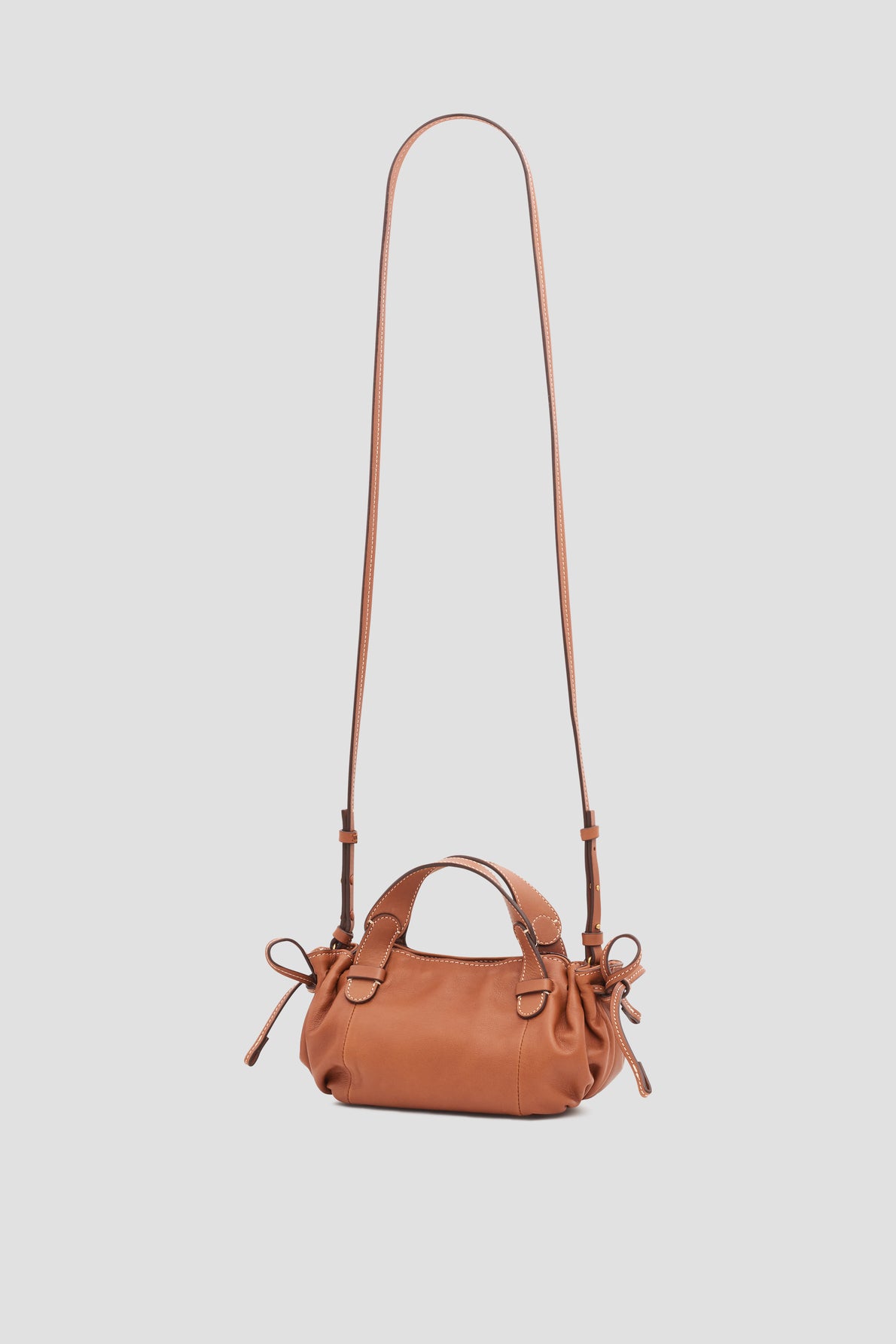 A small brown leather sac bandoulière cuir handbag with a long adjustable shoulder strap, short handles, and side drawstring details, displayed against a plain light background.