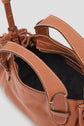 Close-up of a brown leather sac bandoulière cuir with visible stitching, dual handles, gold zipper, and black fabric interior. The top of the bag is open, showing part of the inner compartment and strap details—a refined accessory from the collaboration Merci Micro 24 collection.