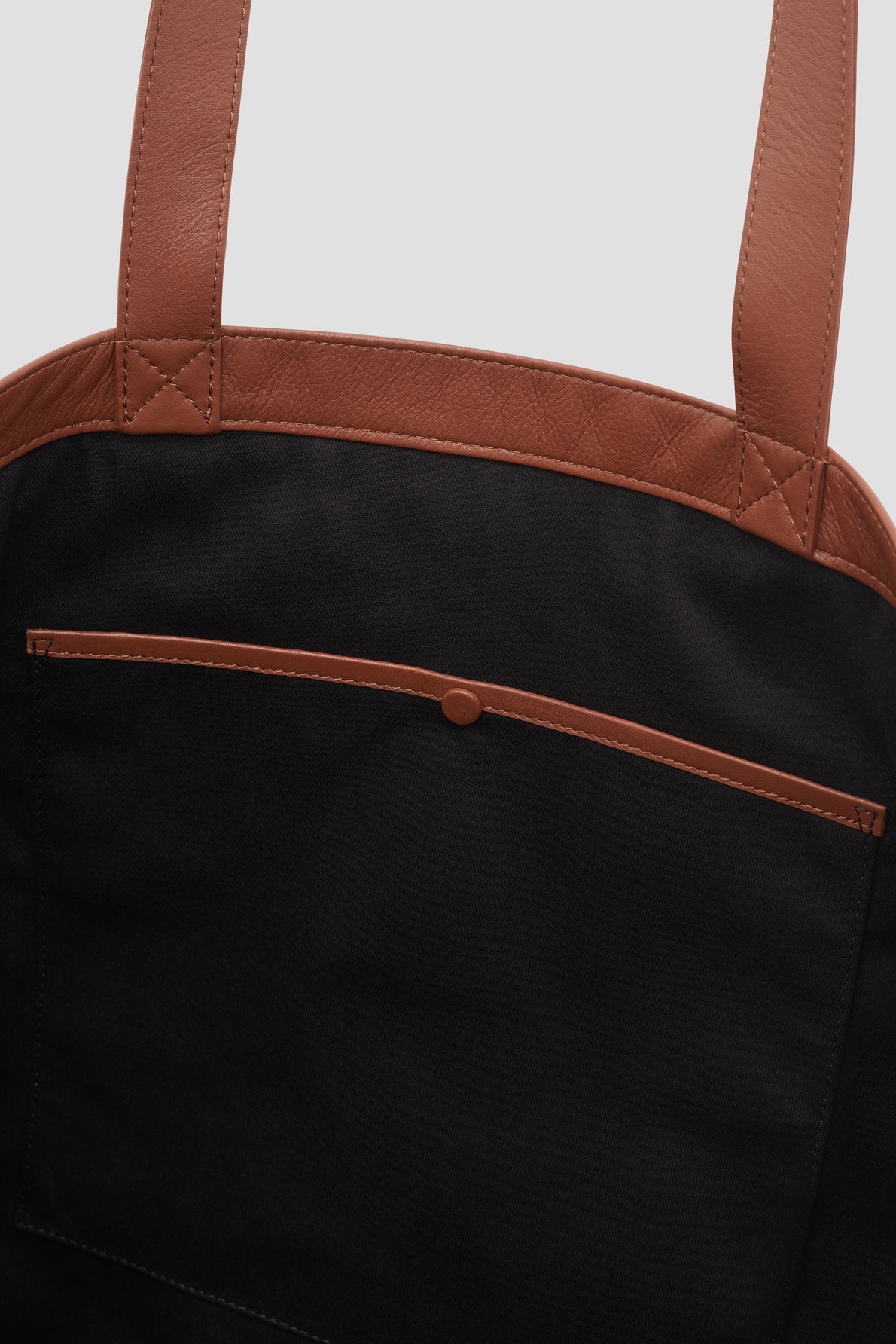 Close-up of a black fabric tote bag cuir with brown leather handles and trim, reminiscent of the elegant styles from Merci Paris and Gérard Darel. The bag features a front pocket with a brown snap button closure.