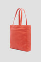A coral-colored leather tote bag from Gérard Darel, featuring two handles, is elegantly angled to reveal its side and front against a plain light background—a timeless tote bag cuir inspired by the effortless style of Merci Paris.