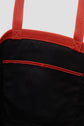 Close-up of a Gérard Darel black fabric tote bag cuir featuring red leather handles and trim. A red button secures the pocket, which is outlined with red stitching. The background is a plain light gray.