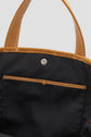 Close-up of an open black cabas Gérard Darel tote bag with brown leather handles and trim in cuir velours, showing a snap button closure and an interior pocket with brown stitching.