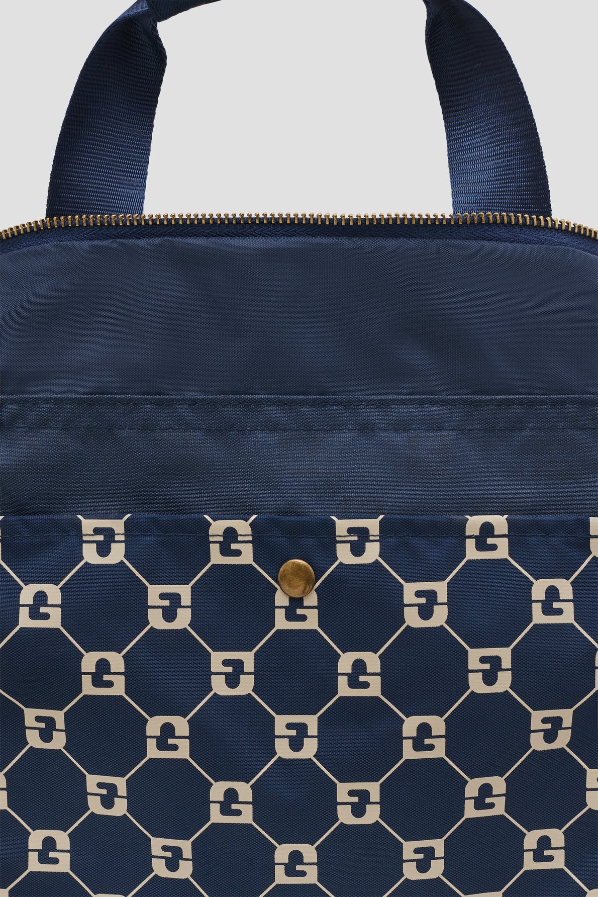 A close-up of a navy blue sac unisexe bag with a gold zipper, navy handle, and a geometric pattern of cream octagons featuring interlocking G designs and a gold button on the front pocket.