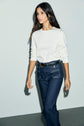 A person with long dark hair wearing a coton épais tee-shirt Bara à manches longues and high-waisted dark blue jeans walks against a plain light background.