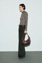 Woman standing in profile, wearing a t-shirt col roulé with a motif imprimé, paired with dark wide-leg pants and holding a large brown handbag, against a plain light background.