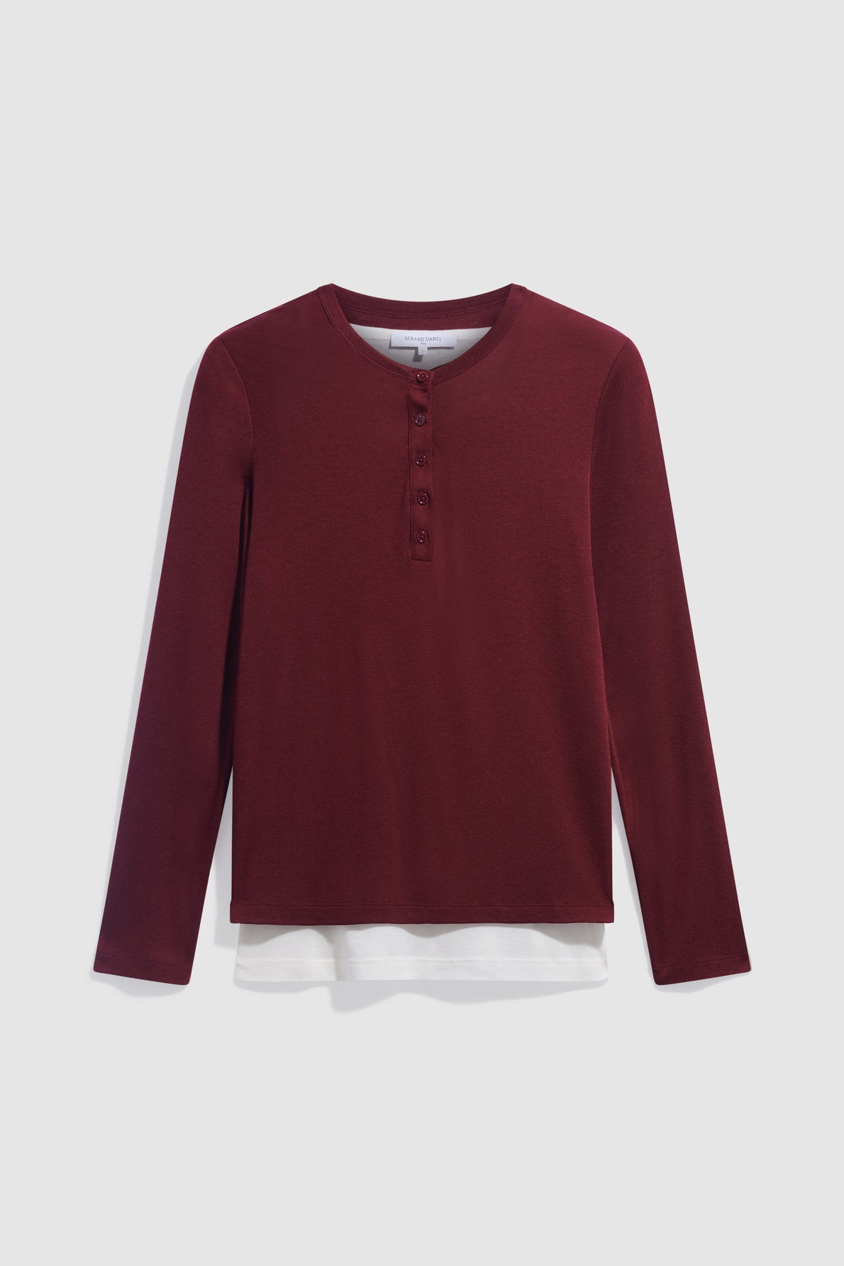 A long-sleeve, bordeaux henley shirt in maille fine with four buttons on the placket, layered over a débardeur blanc, displayed on a plain white background.