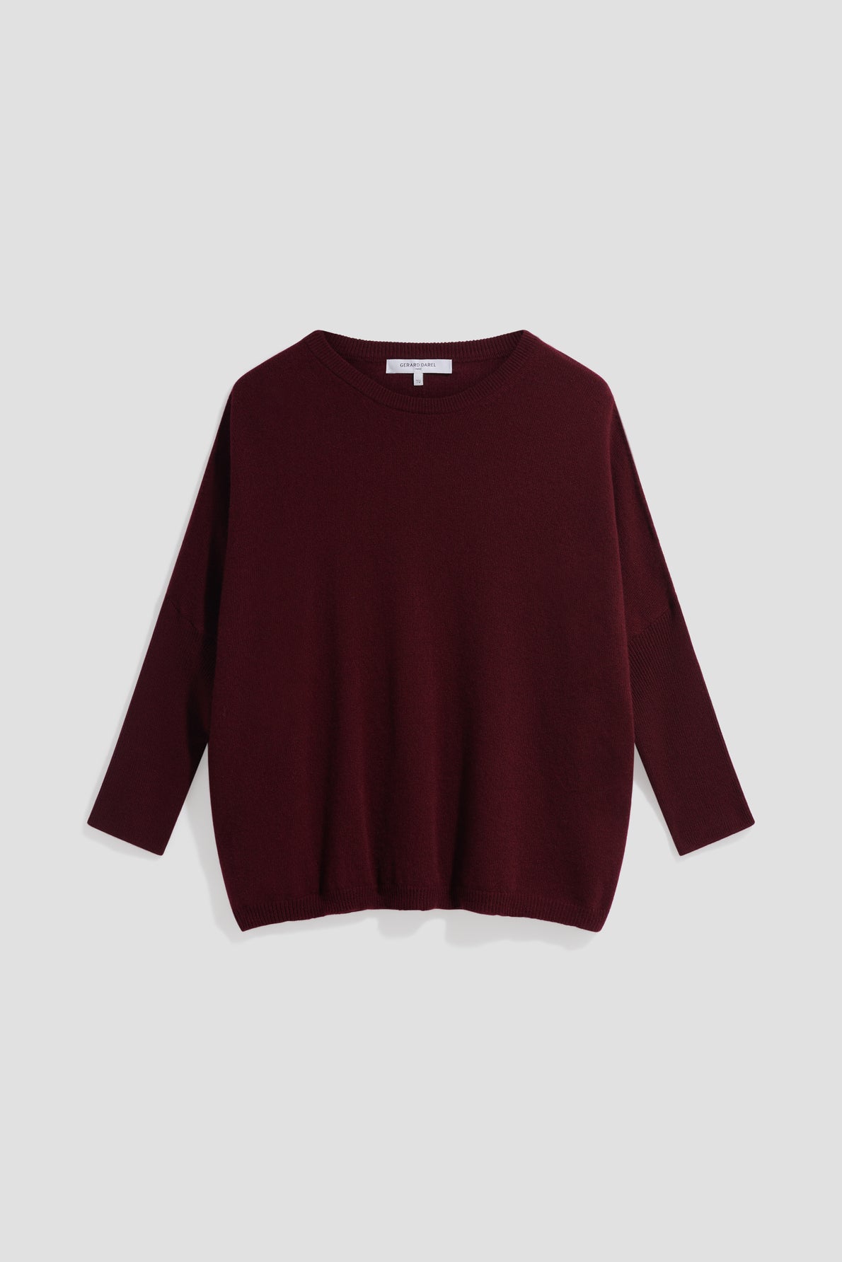 A loose-fitting, long-sleeve, dark burgundy pull en cachemire with a crew neckline is displayed flat against a light gray background.