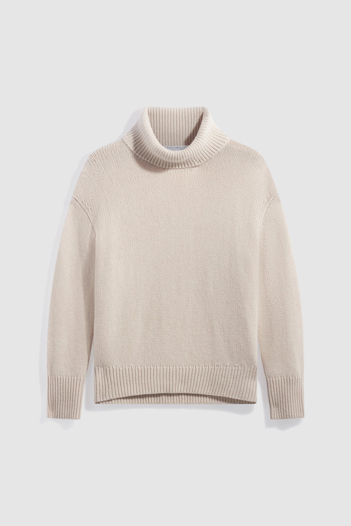 A beige, long-sleeve, col roulé sweater is laid flat on a light background. The pull cachemire features ribbed cuffs, hem, and collar, with a simple and cozy design.