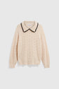 Cream-colored pull maille crochet sweater in soft laine, featuring a textured pattern and a chic col polo with a scalloped collar edged in black. The sweater has long sleeves with ribbed cuffs and hem, displayed on a plain white background.