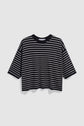 A loose-fitting, black T-shirt with white horizontal stripes and short sleeves, reminiscent of a pull noir écru style, is displayed against a plain, light grey background.