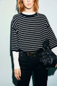 A person wearing a pull rayé laine—an oversized, black and écru striped sweater—paired with black pants and holding a black leather bag, stands against a light background. Their face is partially out of the frame.
