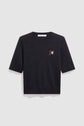 A black pull en laine à col rond with short sleeves, featuring a small motif fleuri—an embroidered pink flower with green leaves—on the left chest, displayed against a plain light gray background.