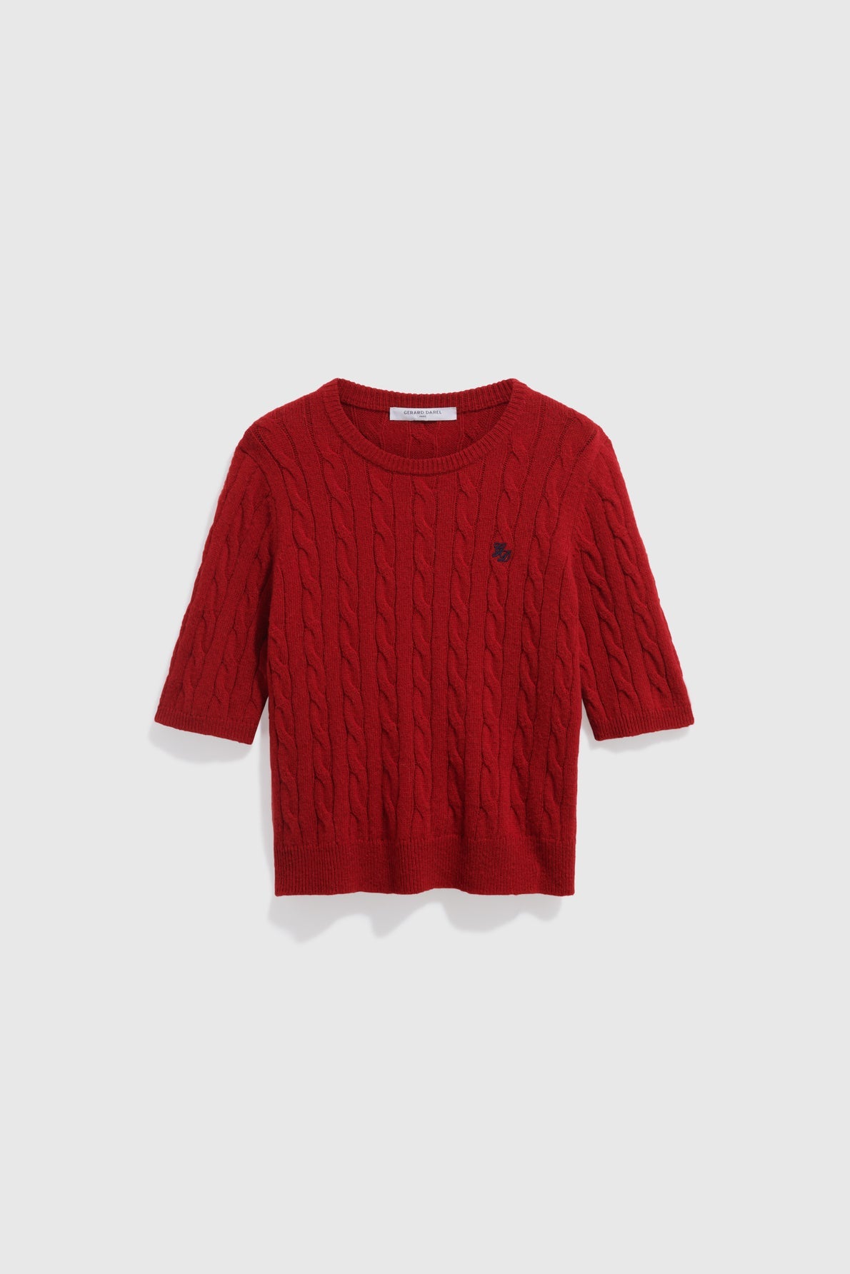 A red, short-sleeved, cable knit sweater crafted from soft laine mérinos with a round neckline and a small embroidered logo on the left chest, displayed on a plain white background.