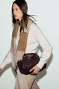 Woman wearing a pull laine femme blanc and beige scarf, holding a dark brown woven leather handbag under her arm, walking against a plain light background.