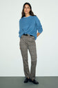 Woman standing against a plain background, wearing a pull bleu intense en laine mohair, plaid pants with a black belt, and black shoes.