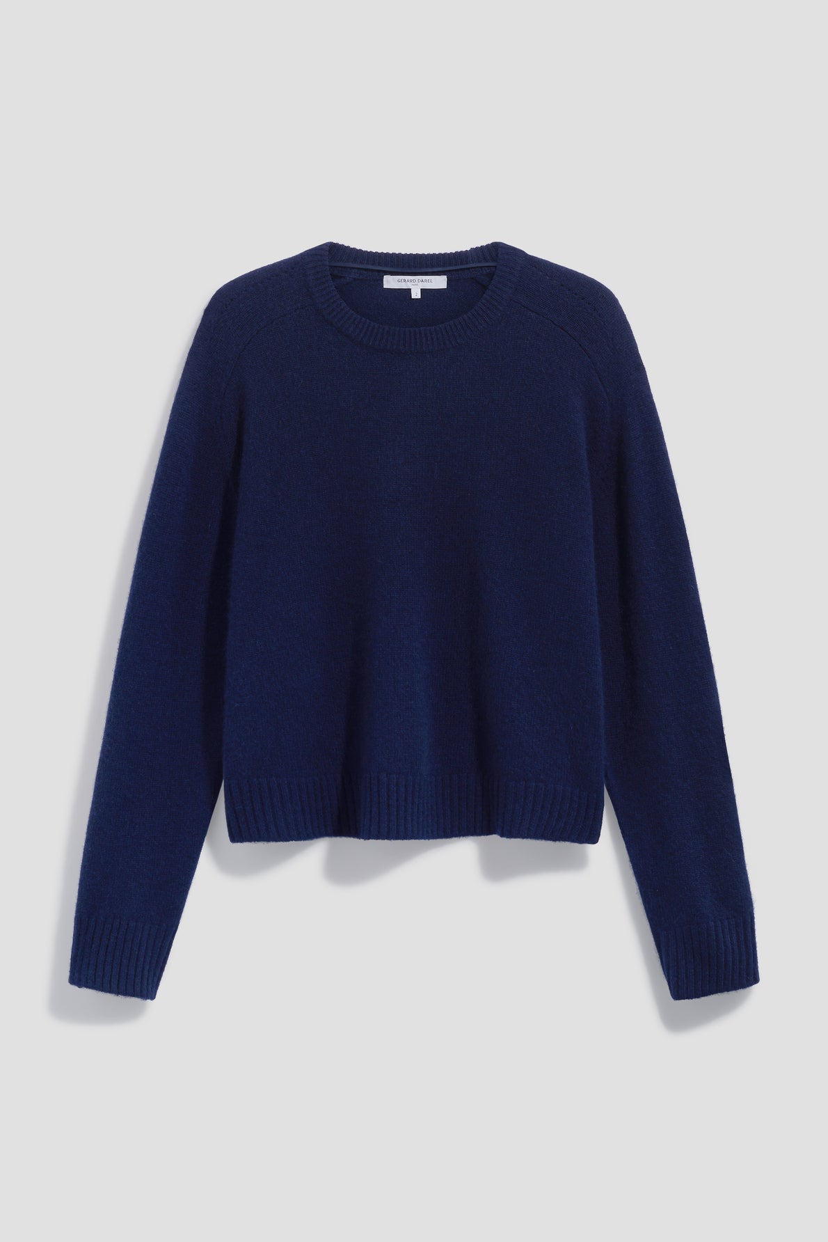 A navy blue, long-sleeve knit pull cachemire with a col rond and ribbed cuffs, hem, and collar, displayed against a light gray background.