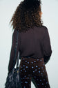 A person with curly hair, seen from behind, wearing a pull marron and brown pants with blue flower patterns, carries a black fringed shoulder bag.