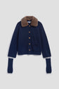 A gilet bleu marine with a luxurious col fausse fourrure in brown, wooden buttons, two front pockets, and extra-long sleeves with thumb holes, displayed on a plain white background.