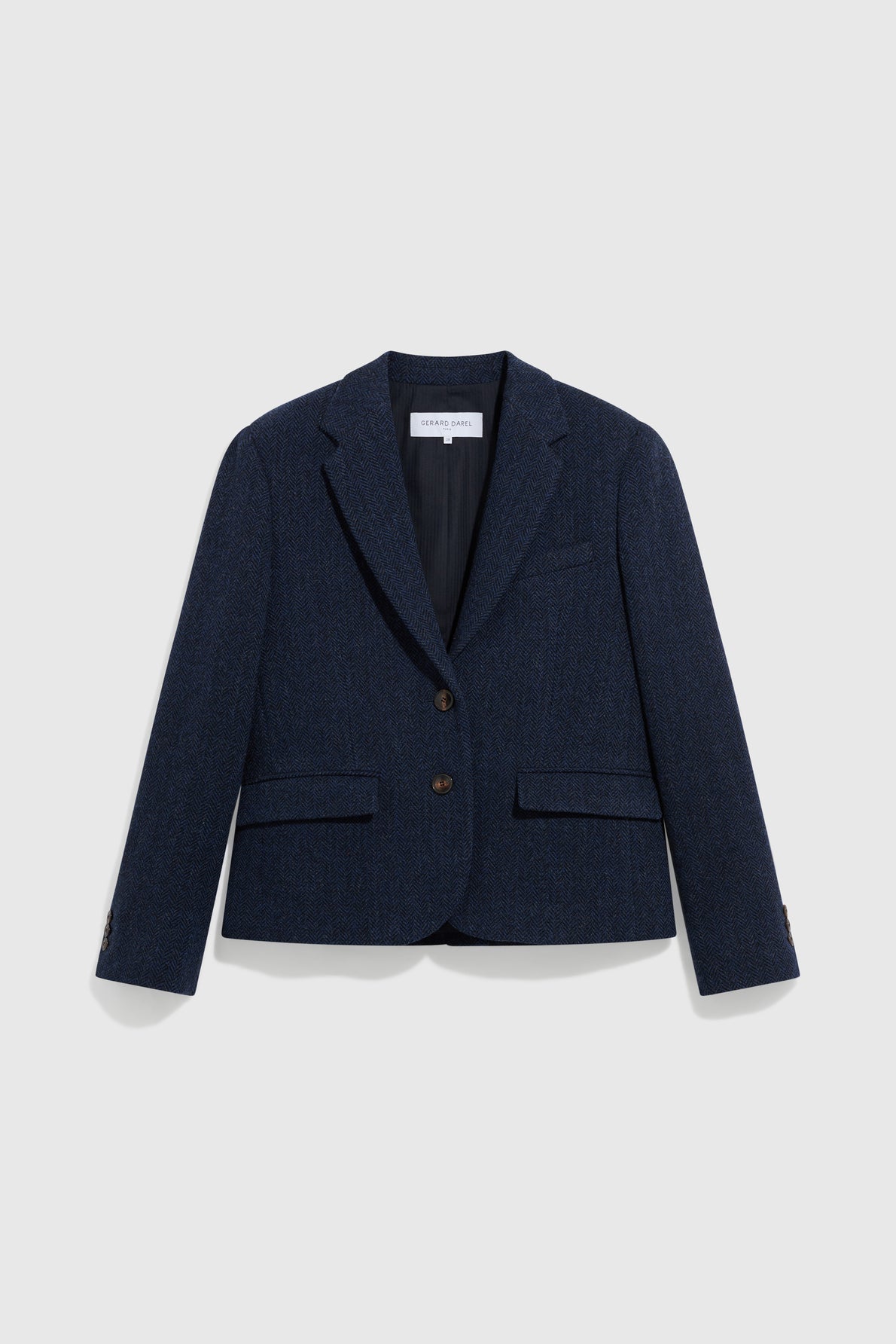 A navy blue veste tailleur femme with two front buttons, notched lapels, and two flap pockets, crafted from fine laine vierge and displayed on a plain light grey background.