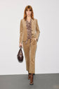 A person with shoulder-length hair wears a veste tailleur velours tan corduroy suit, a patterned blouse, and brown boots, carrying a large brown handbag, walking against a plain white background.
