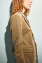 A woman with wavy red hair wearing a veste chic décontractée—a tan corduroy blazer—and a patterned shirt stands against a light background, facing sideways.